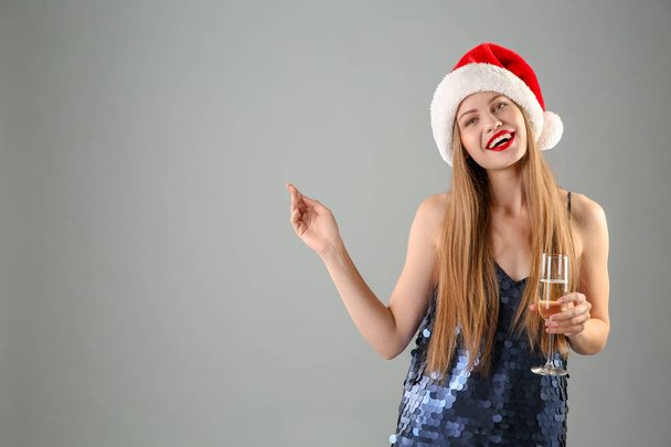 Young beautiful woman in Santa hat with glass of champagne on grey background. Christmas celebration - Fotó, kép
