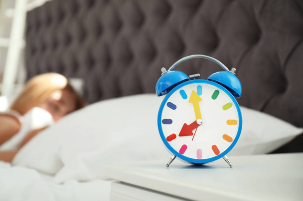 Reloj despertador analógico y mujer somnolienta borrosa en el fondo. Hora del día
 - Foto, Imagen
