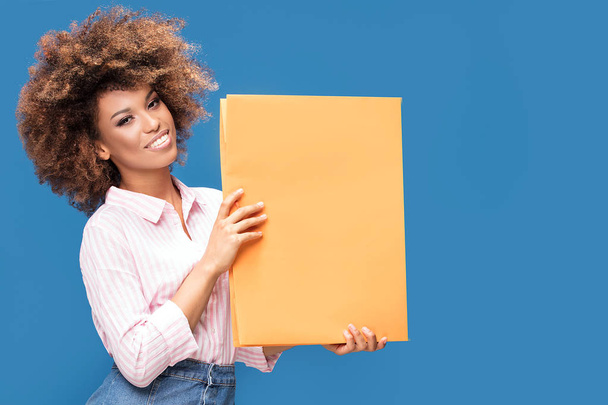 Cheerful afro american woman showing blank yellow board over blue background. - 写真・画像