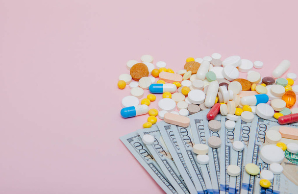 Dollars and pills on a pink background. Prescription medicine on dollars for pharmaceutical industry concept of high cost for healthcare and medication, top view. - 写真・画像