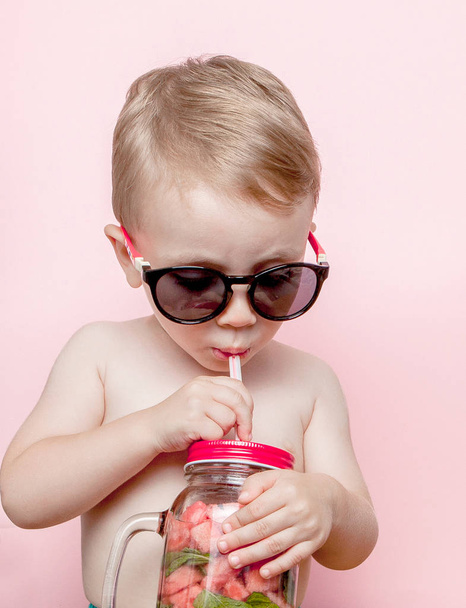 Little boy drinking fresh lemonade with piece of watermelon and ice on pink background. - Zdjęcie, obraz