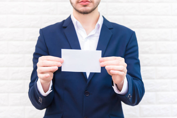 Business man showing white paper. Man  wearing blue suit and holding white blank card. Lifestyle and working concept. Business and object theme. Blank space in paper for insert text. - Foto, afbeelding