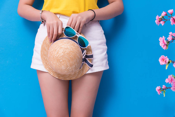 Closeup of Beauty woman posing with sunglasses and straw hat in front of blue wall background. Summer and vintage concept. Happiness lifestyle and people portrait theme. Cute pastel tone. Lower body - Photo, Image