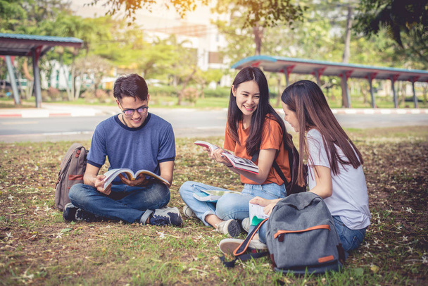 Group of Asian college student reading books and tutoring special class for exam on grass field at outdoors. Happiness and Education learning concept. Back to school concept. Teen and people theme. - Photo, Image
