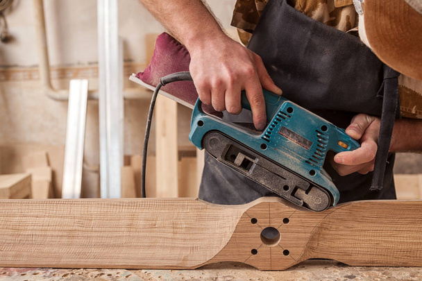Close up of an young man builder carpenter equals polishes wooden board with a  random orbit sander  in the workshop - Fotografie, Obrázek