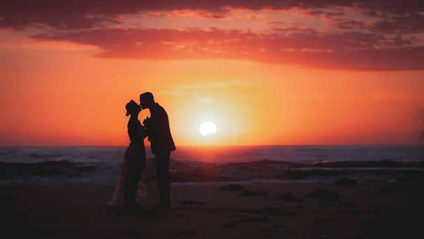 σιλουέτα του ζευγάρι εραστών, νύφη και τον γαμπρό, κρατώντας τα χέρια κατά τη διάρκεια περιόδου Ανατολή του ηλίου στην παραλία με την όμορφη ανατολή του ηλίου ροζ ουρανός. - Φωτογραφία, εικόνα