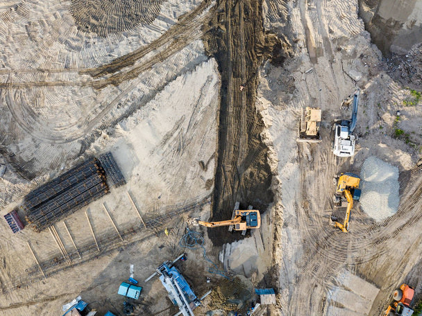Vue aérienne du site de construction au stade initial de la construction et de la préparation du sol avec une plate-forme de forage, des pelles et trois camions en attente de chargement du sol pour le transport
 - Photo, image