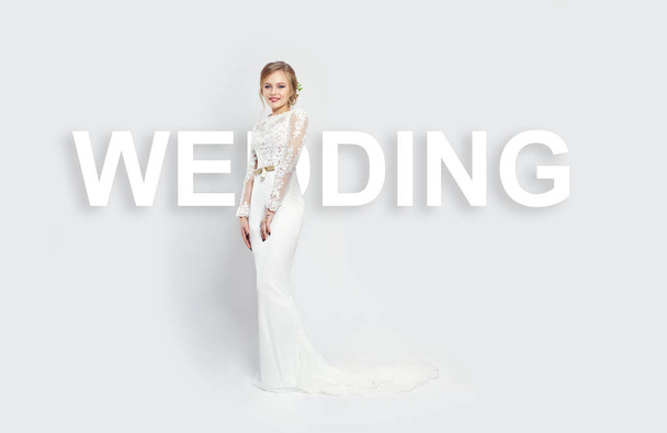 Inscription wedding is located behind a woman in a white dress on a white background in the Studio. Bride girl smiles in a beautiful long dress, perfect hairstyle. Word wedding, wedding Agency - Photo, image