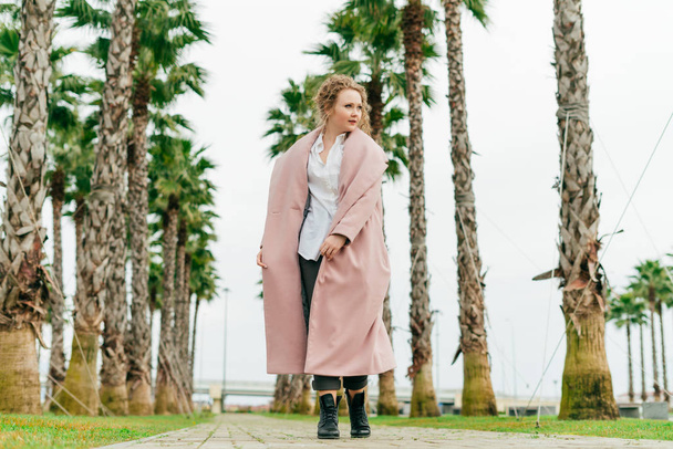 stylish curly woman in a long pink coat enjoying the warm spring weather in the park - Foto, Bild