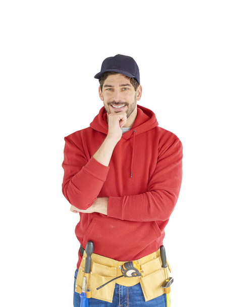 Happy young handyman wearing baseball cap and hoodie while standing at isolated white background wiht hand on his chin. - 写真・画像