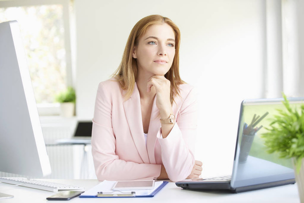 Portrait of beautiful young businesswoman sitting at modern office and and looking thoughtfully while working on laptop.  - Foto, Bild