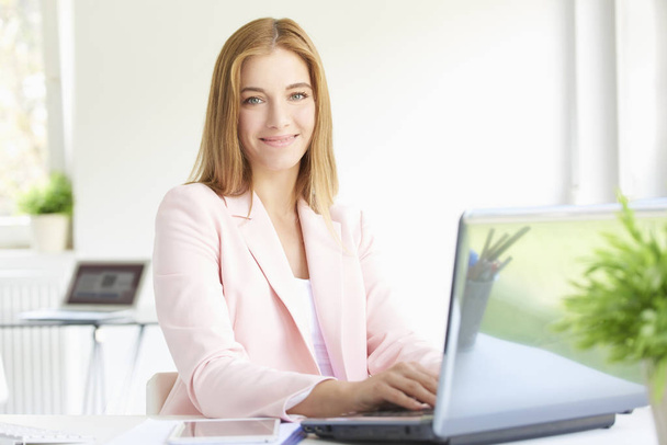 Close-up portrait of beautiful young smiling financial assistant businesswoman sitting at modern office and working on laptop.  - Foto, imagen