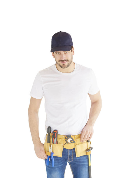 Portrait of handsome young handyman wearing baseball cap and tool belt while standing at isolated white background with copy space. - Foto, Bild