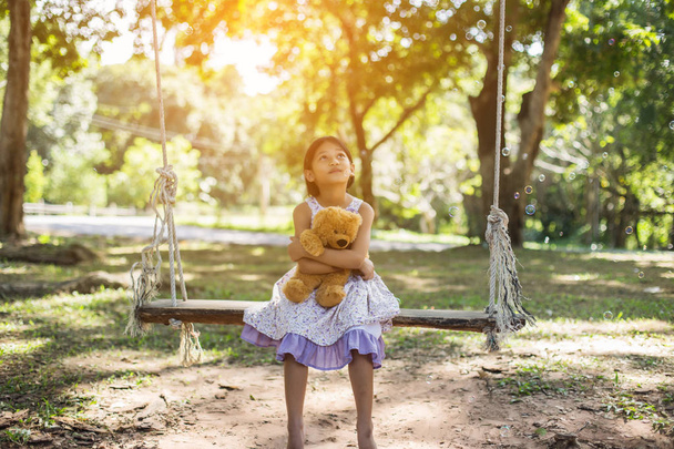 Cute little girl sitting swings , teddy bear sitting with her,little girl pointed to the tree. - Fotó, kép