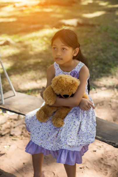 Jolie petite fille assise balançoires, ours en peluche assis avec elle, petite fille pointée vers l'arbre
. - Photo, image