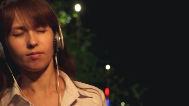 Dziewczyna w słuchawkach z długich włosów i dotykowy telefon taniec uśmiechający się i słuchanie muzyki w nocy w parku. Szczelnie-do góry - Materiał filmowy, wideo