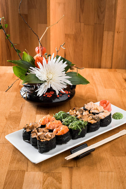 Gunkan sushi set with salmon, eel, chukka, shrimp and chicken meat on a white plate among flowers. wooden bacground. Traditional Japanese cuisine. close up - Photo, Image
