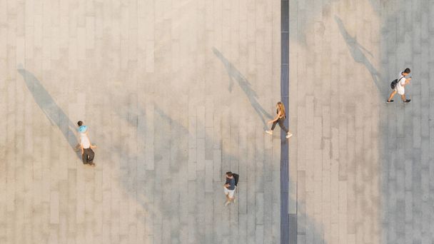 people walk on across the pedestrian concrete landscape with black silhouette shadow on ground (top aerial view) - Photo, Image