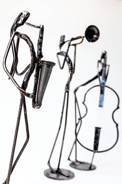 Фигуры музыкальных исполнителей, сделанные из сварной черной металлической проволоки. Скрипач, трубач и саксофонист играют вместе. Живые линии
 - Фото, изображение