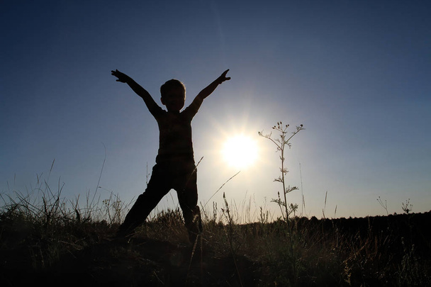 Σιλουέτα ενός αγοριού με τα χέρια του επάνω στη στάση ενός ανθρώπου rune. Το παιδί χαρά συναντά την αυγή της την Ανατολή του ηλίου. - Φωτογραφία, εικόνα