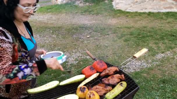 Volwassen vrouw bereidt een ingemaakte smakelijke varkensvlees of rundvlees vlees en groenten op een barbecue of op de grill. - Video