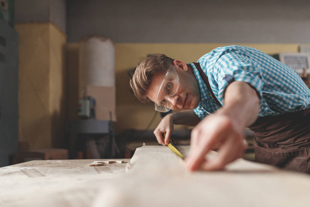 Young master measuring a board in carpentry - Foto, Bild