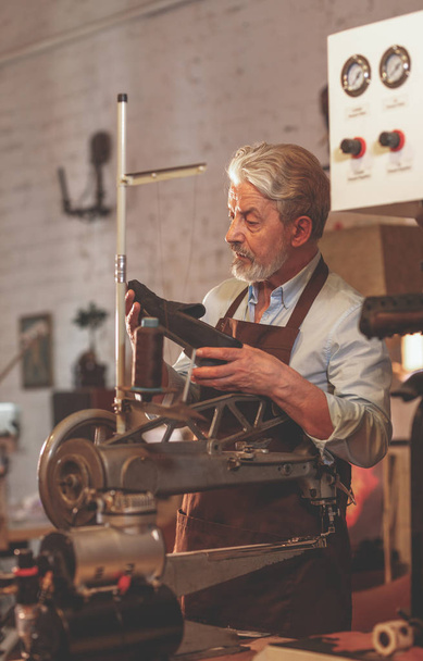 Een oudere man met een schoen in een workshop - Foto, afbeelding