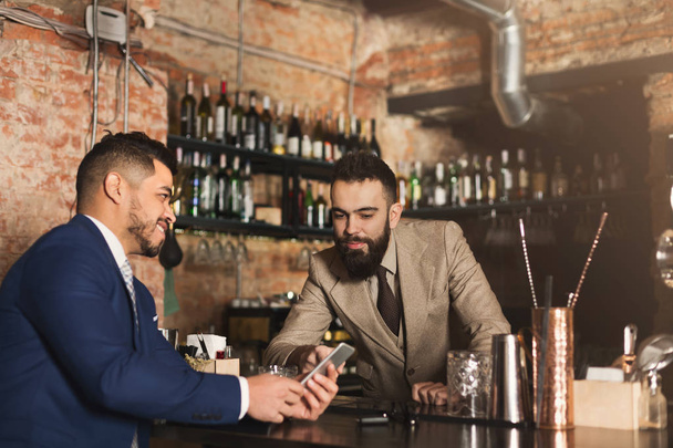 Homme d'affaires montrant des informations au téléphone au barman
 - Photo, image