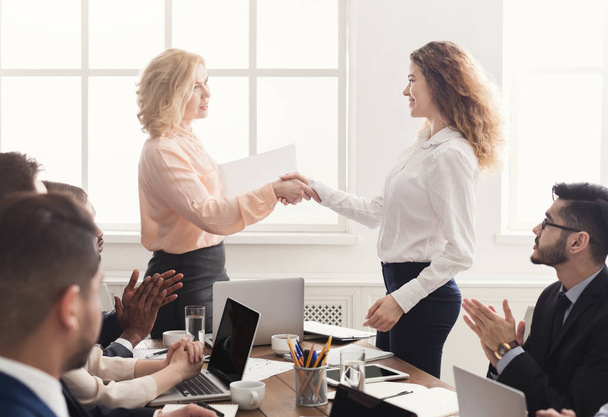 Smiling boss shaking hand of cheerful happy female employee, rewarding excited worker or congratulating partner with achievement, team applauding - Foto, imagen