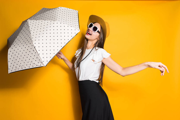stylish cheerful young girl in trendy hat and sunglasses holds umbrella and poses - Zdjęcie, obraz