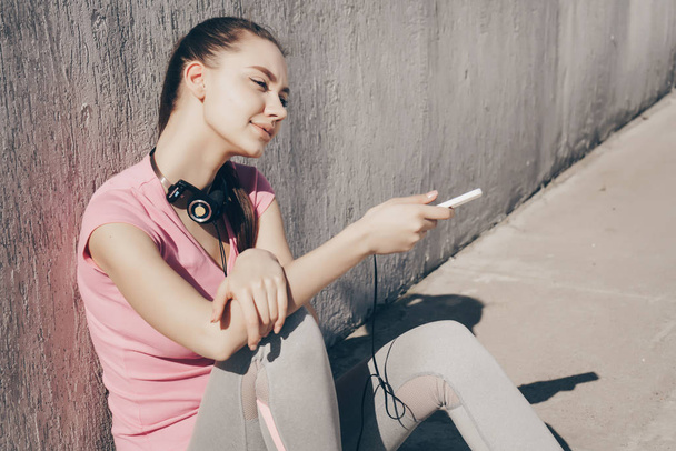 sports young girl in a pink T-shirt resting in the sun after running, holding the phone in her hand - Φωτογραφία, εικόνα
