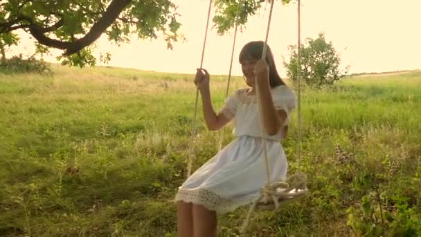 Nastoletnie dziewczyny z długimi włosami w białej sukni, śmieje się toczenia na huśtawce pod drzewem Dąb letni w sezonie ciepłe. Zwolnionym tempie. - Materiał filmowy, wideo