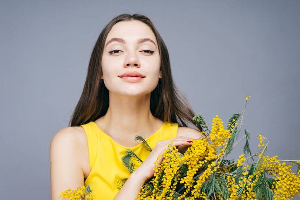 confident beautiful girl posing, looking at the camera, holding a bouquet of spring yellow mimosa - Foto, afbeelding