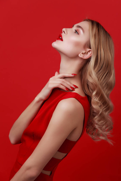 Studio shot of fashionable blonde woman in red dress. hollywood hairstyle and red lips. red nails. curly fashion model with glamour make-up. young woman on red background.  - Фото, изображение