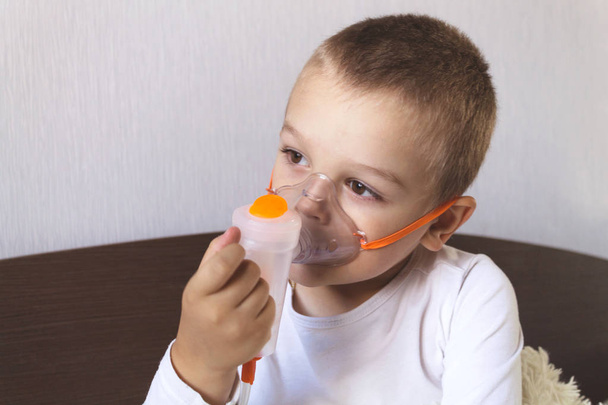 A child inhales a nebulizer at home on the bed - 写真・画像