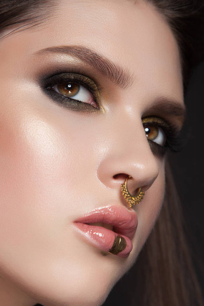 beauty close-up. amazing young model with green smoky eye make-up. creative fashion look. brunette isolated on black. gold paint on her neck. fake nose piersing - Photo, Image