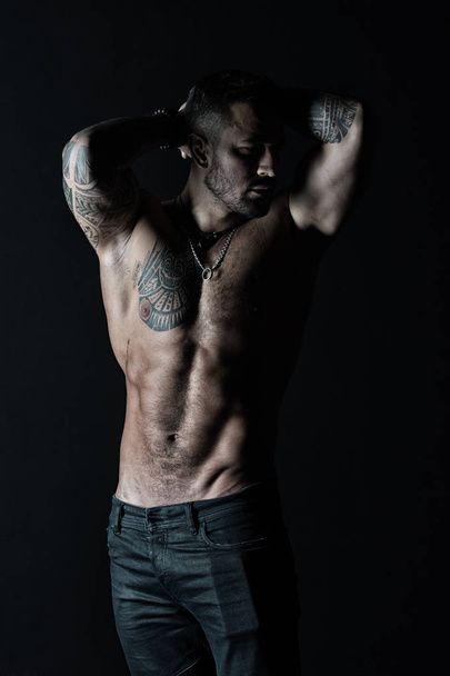 Sportsman with six pack and ab. Tattooed man show sexy muscular torso. Bodybuilder with biceps and triceps. Fashion model with tattoo in jeans. Bodycare with fitness and sport in vintage filter - Фото, изображение