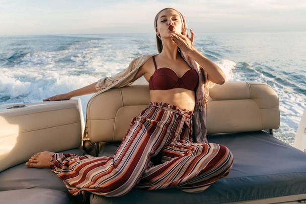 beautiful stylish girl in fashionable clothes posing on her yacht, sends an air kiss - Фото, зображення