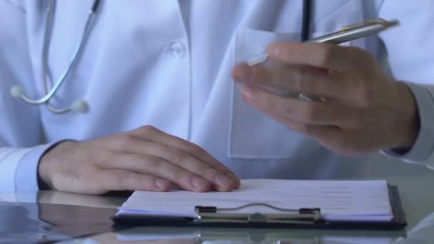 Young male doctor filling patient card, writing down illness symptoms, diagnosis - Video, Çekim