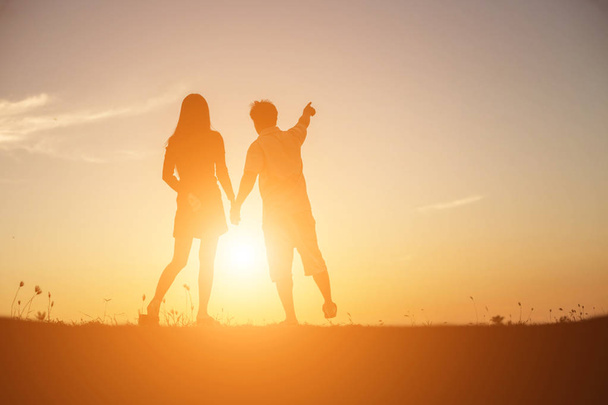  Silhouette eines Mannes und einer Frau, die sich an den Händen halten und zusammen gehen. - Foto, Bild