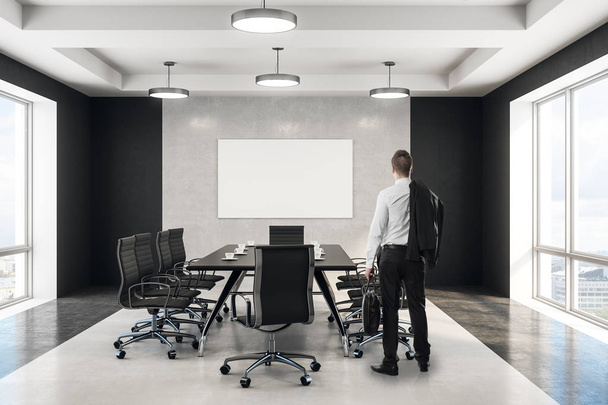 Представьте бизнесмена, стоящего возле черного стола для совещаний в конференц-зале с пустым белым плакатом посреди бетонной стены. 3d-рендеринг
 - Фото, изображение