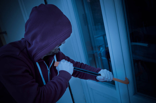 Bluza z kapturem włamywacza zmuszając okno blokady do kradzieży w domu w nocy - Zdjęcie, obraz