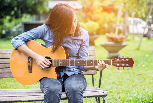 Όμορφη νεαρή γυναίκα που παίζει κιθάρα που κάθεται στον πάγκο, ευτυχισμένη στιγμή έννοια. - Φωτογραφία, εικόνα