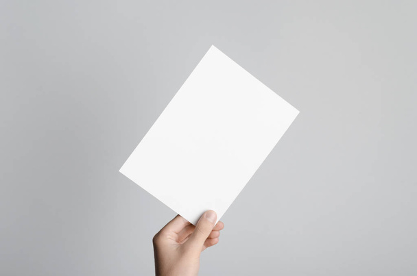 A5 Flyer / Invitation Mock-Up - Male hands holding a blank flyer on a gray background. - 写真・画像
