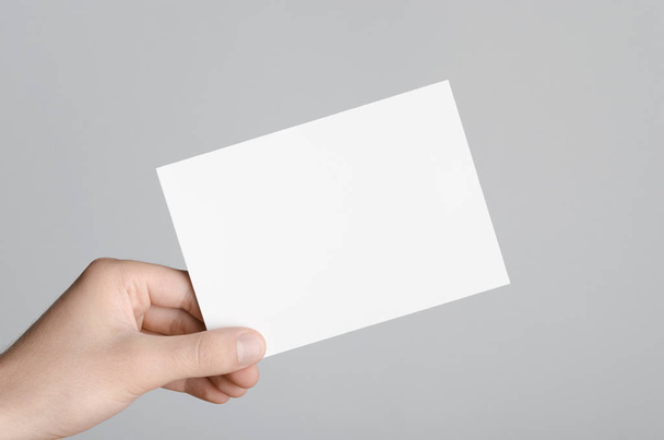 a6 Flyer / Postkarte / Einladungsmock-up - männliche Hände mit einem leeren Flyer auf grauem Hintergrund. - Foto, Bild