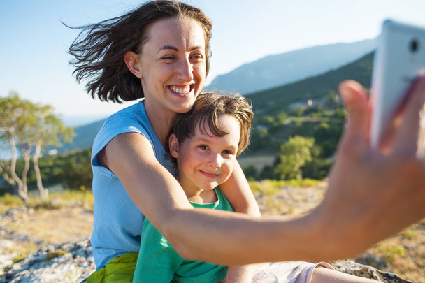 Una mujer con un niño en la cima de una montaña. Mamá y su hijo hacen selfie en el fondo de un hermoso paisaje. Viajar con un niño
. - Foto, Imagen