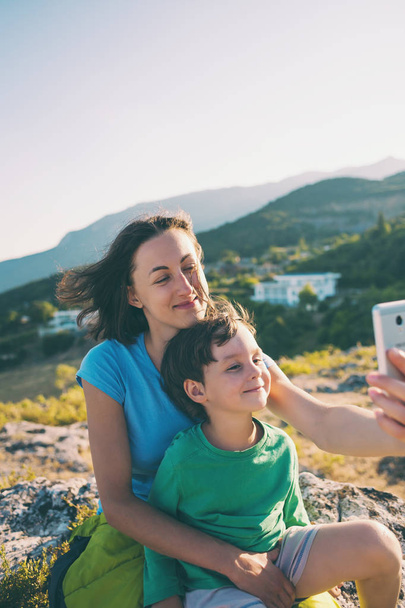 Kobieta z chłopakiem na szczycie góry. Mama i jej syn zrobić selfie na tle pięknego krajobrazu. Podróżując z dzieckiem. - Zdjęcie, obraz