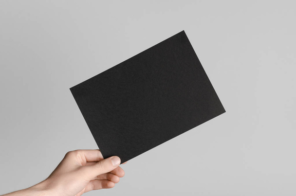 Black A5 Flyer / Invitation Mock-Up - Male hands holding a black flyer on a gray background. - Foto, Imagem