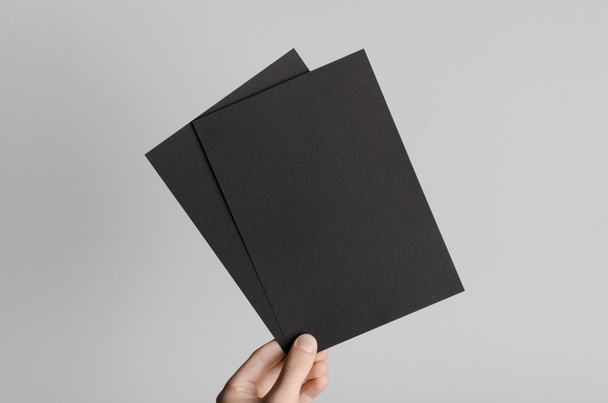 Black A5 Flyer / Invitation Mock-Up - Male hands holding black flyers on a gray background. - Φωτογραφία, εικόνα