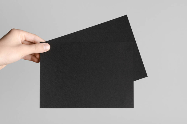 Black A5 Flyer / Invitation Mock-Up - Male hands holding black flyers on a gray background. - Foto, Bild